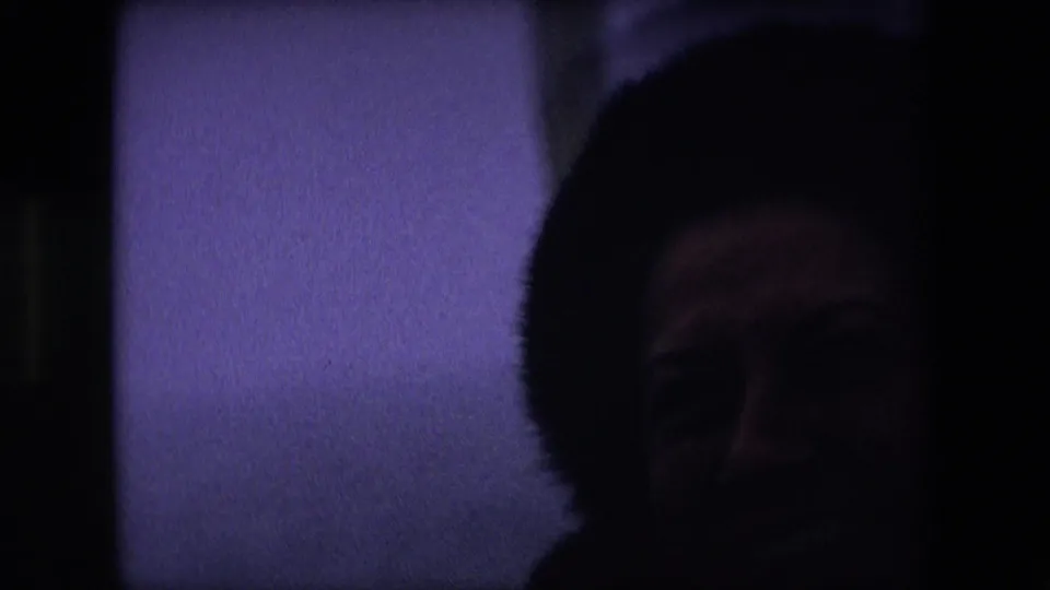 The woman appears in a darker, underexposed 1967 Calais home-movie frame, her fur hat and face visible against a pale shipboard or water background.