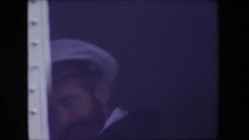 A brief 1967 Calais home-movie frame shows a man in a sailor-style white cap and dark uniform, partly obscured by soft exposure and film texture.