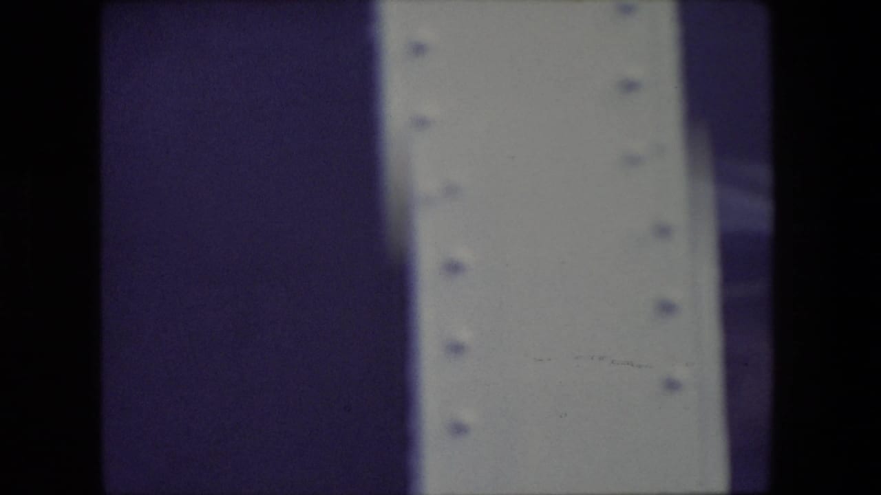 Dark vertical film edge beside a pale riveted surface and purple-toned strip.