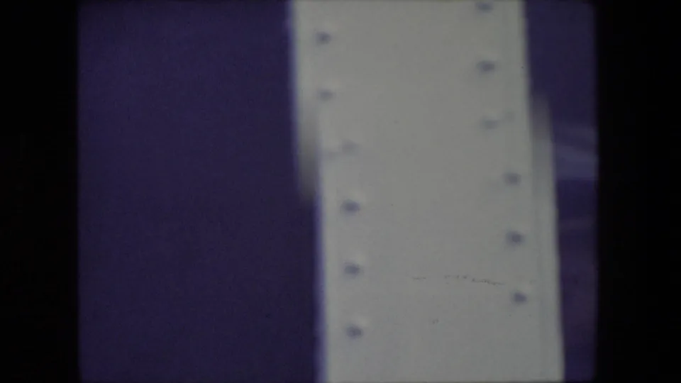 Abstract-looking 8mm frame with a dark central film edge, a pale riveted vertical surface, and purple color shift, likely between visible subjects.
