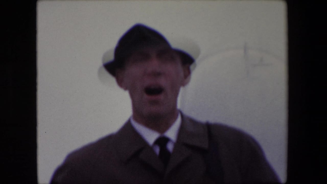 Man in a dark hat and coat facing the camera with his mouth open.