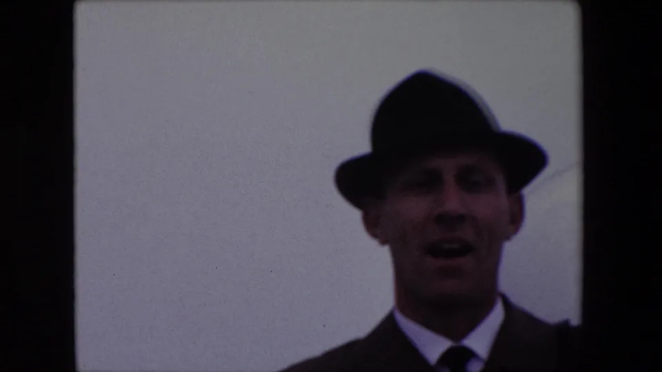 A soft 8mm frame from the 1967 Calais clip shows the man closer in the lower portion of the contact sheet, wearing a dark fedora and suit while opening his mouth toward the camera.