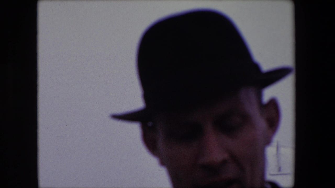 Shadowed man in a dark fedora leaning near the camera inside a divided window frame.