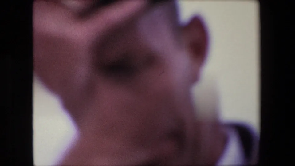A very soft, close home-movie view shows an adult face near the camera, with facial detail obscured by motion blur, exposure, and 8mm grain.