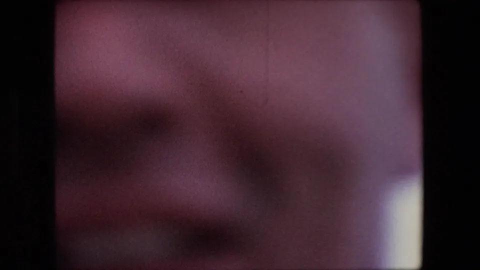 A blurred hand or wrist passes close to the 8mm camera, creating a reddish soft foreground shape during the informal travel shot.