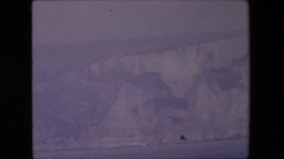 A distant hazy cliff or coastal landform fills the lower frame in the metadata-supported Calais travel footage, rendered with muted purple 8mm color and grain.