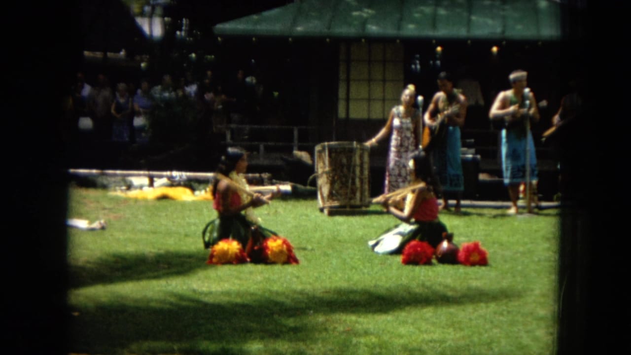 1967 Hawaii Super 8 frame showing women performing hula on a lawn while musicians play behind them and a crowd watches from the edges.