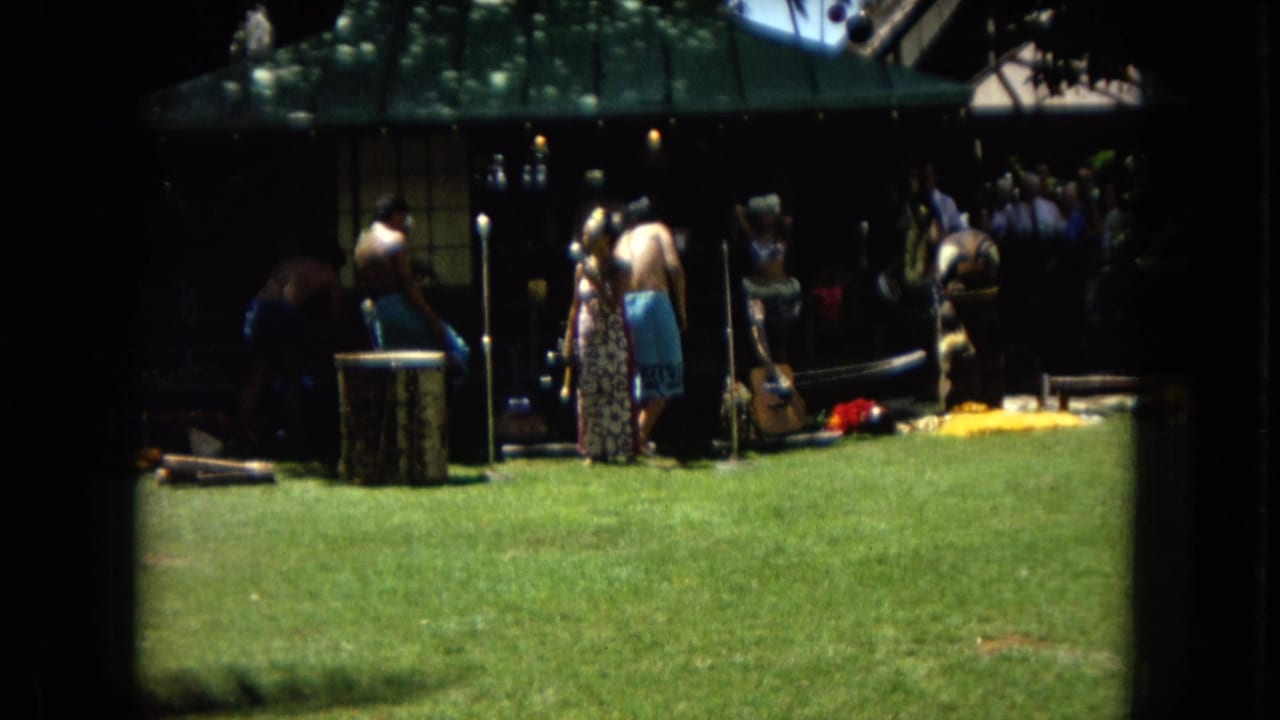 Outdoor performance area with people gathered near musicians under shade.