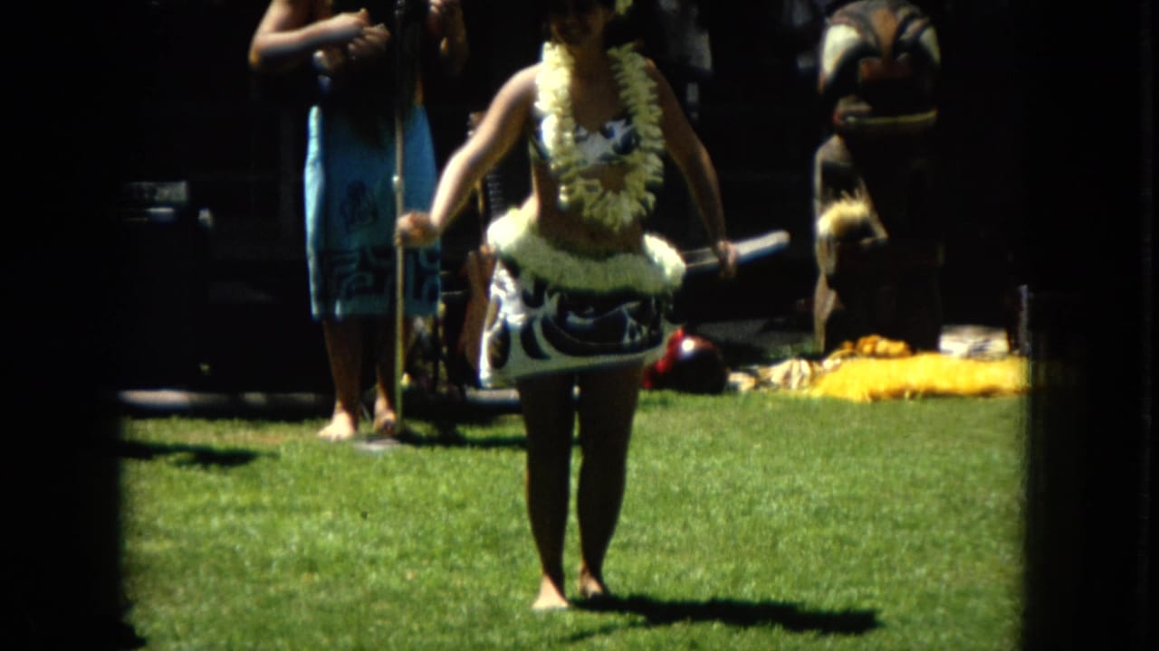 Dancer centered on a lawn with musicians and instruments in the background.