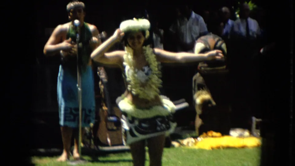 1967 Hawaii Super 8 frame showing a hula dancer with one arm extended near a microphone stand as a musician or singer performs behind her.
