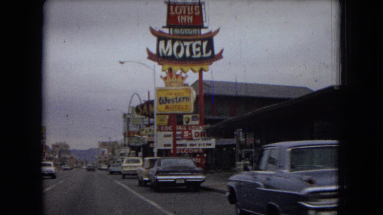 1967 Las Vegas street view from a moving vehicle, with large motel signs, mid-century cars, and commercial storefronts along a broad road.
