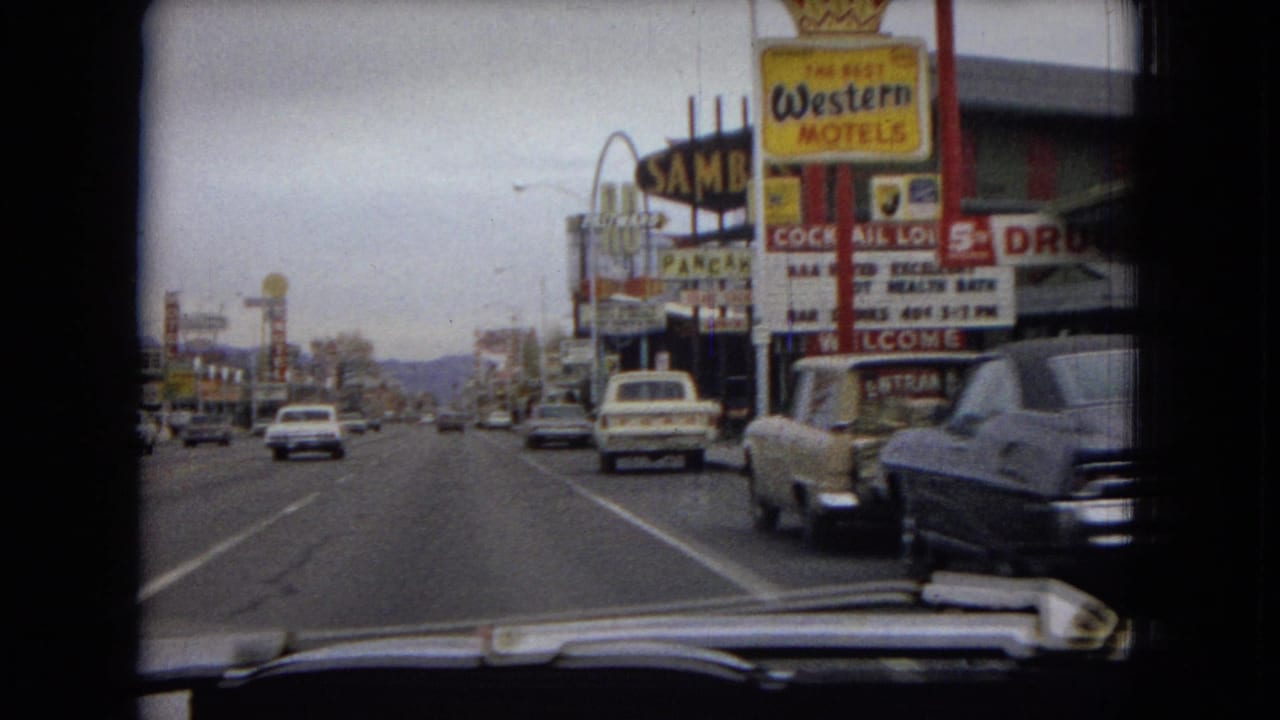 Roadway traffic passing motel and drugstore signs on a commercial street.