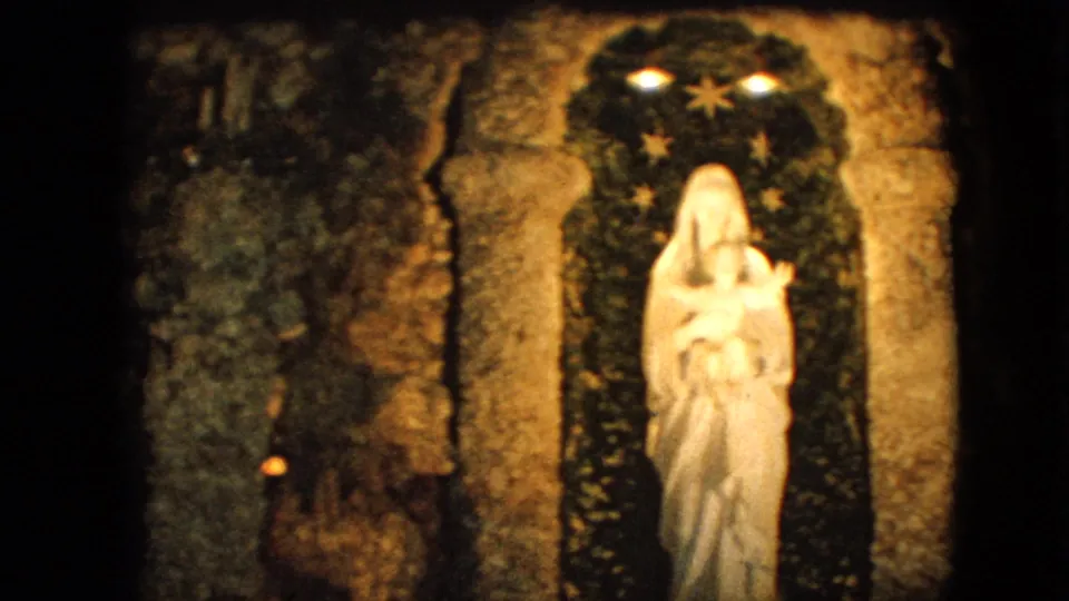 1967 Iowa 8mm frame with a white statue of the Virgin Mary holding the infant Jesus inside a rough stone arch, set against a dark backdrop with stars and small lights.