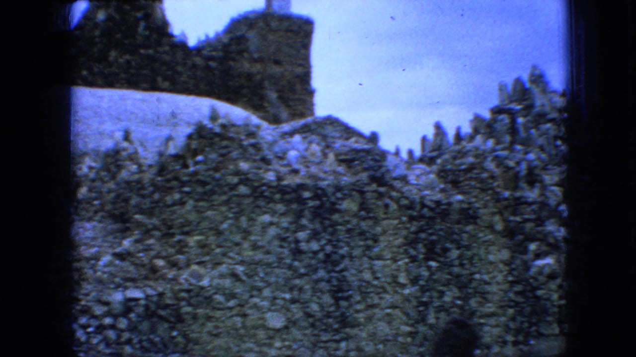 1967 Iowa 8mm frame showing weathered stonework, a rocky mound, and surrounding greenery under a cloudy blue-tinted sky.