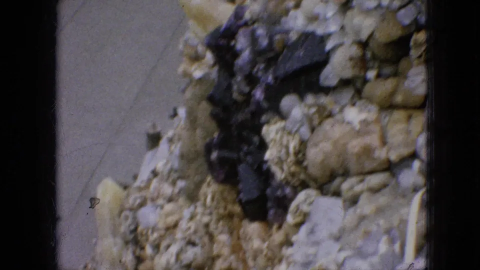1967 Iowa 8mm frame showing a close section of shell-covered stonework, dark embedded material, and the paved garden path below.
