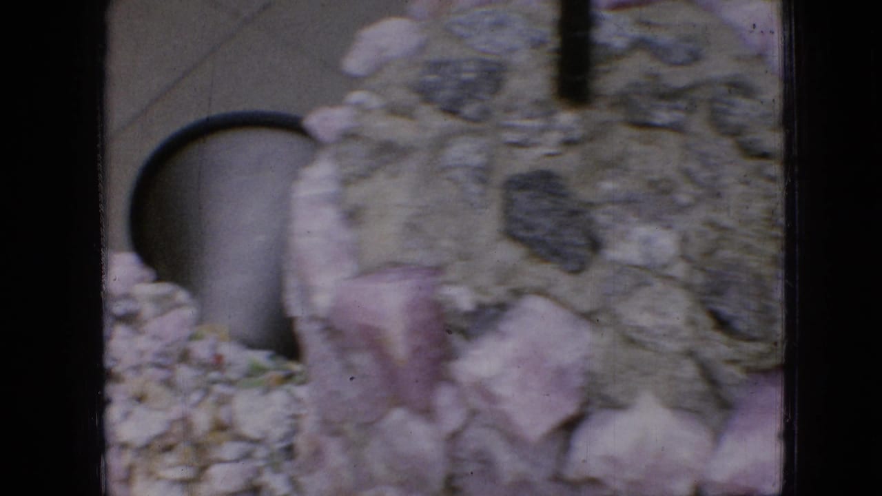 Textured stone wall with dark arched opening and pale rocks.