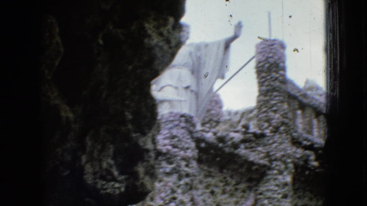 1967 Iowa 8mm frame showing a white robed figure with raised arms above rough stonework, partly obscured by a dark arch-like foreground.