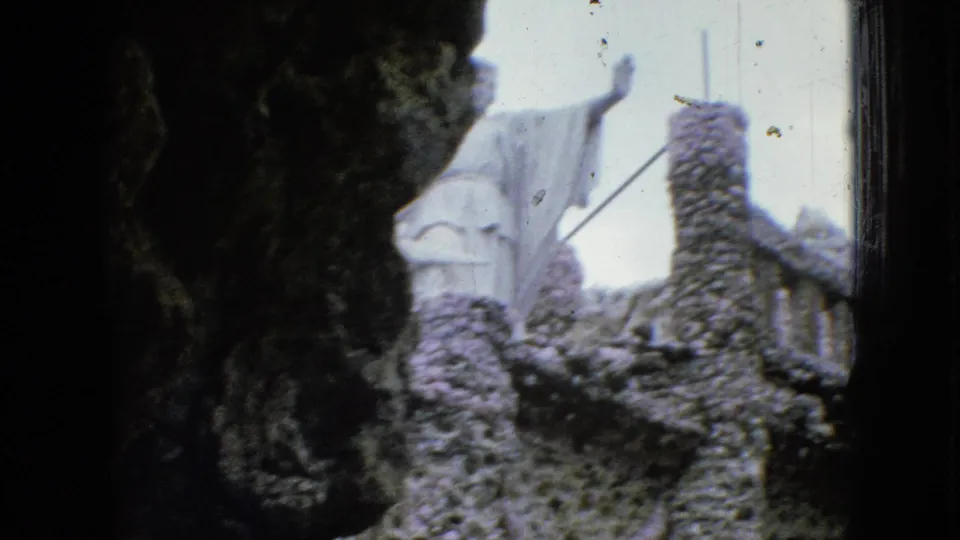1967 Iowa 8mm frame showing a white robed figure with raised arms above rough stonework, partly obscured by a dark arch-like foreground.