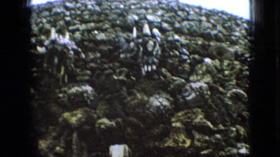 1967 Iowa 8mm frame showing a closer view of the irregular stone surface, with small pale vertical details set into or above the masonry.