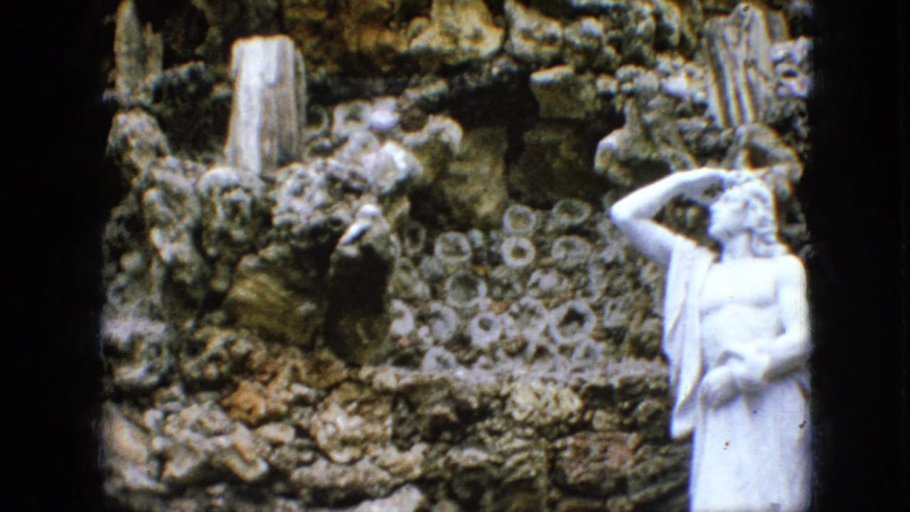 White statue in profile before a dense rock grotto wall with circular stone details.
