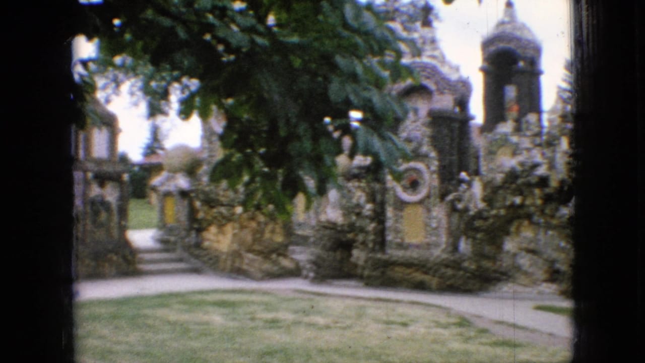 1967 Iowa 8mm frame showing an ornate stone garden structure with arched alcoves, a small tower-like feature, lawn, walkway, and leafy foreground branches.