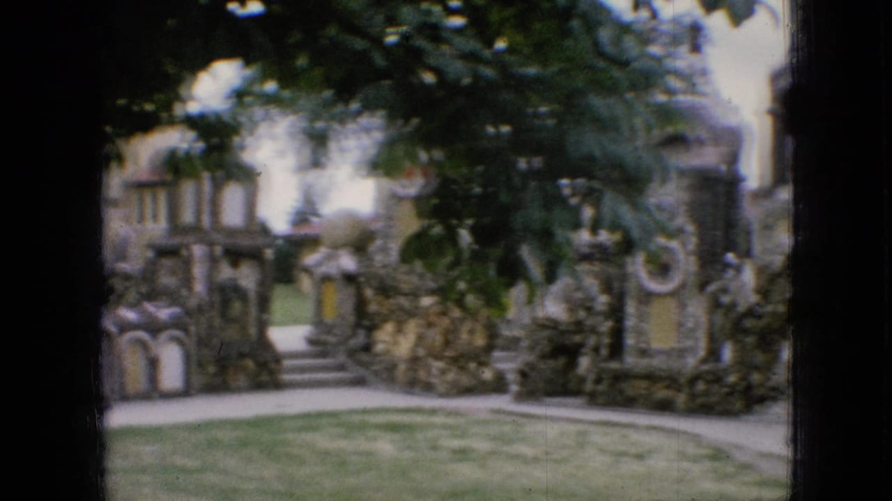 1967 Iowa 8mm frame showing a visitor view of a stone garden walkway with rough walls, arched openings, lawn, and leafy trees.