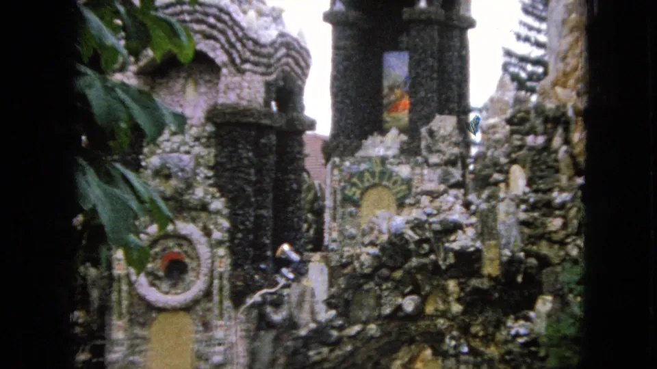 1967 Iowa 8mm frame showing a closer visitor view of weathered stone features, circular decorations, small sculptural details, and a dark arched tower.