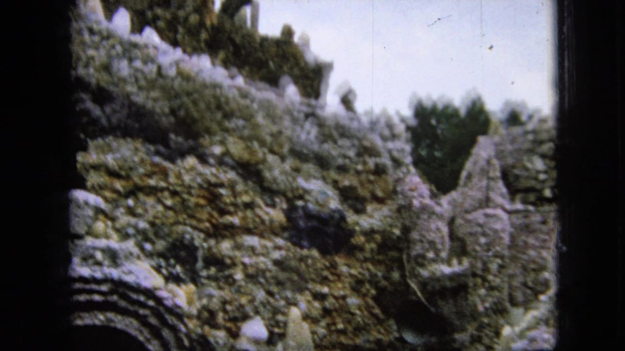 1967 Iowa 8mm frame showing a rough stone grotto wall with uneven masonry, small sculptural forms, and an arched opening at the lower left.