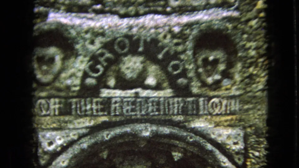 1967 Iowa home-movie frame showing a carved grotto plaque with relief faces, arched lettering, and the partially legible phrase of the Redemption.