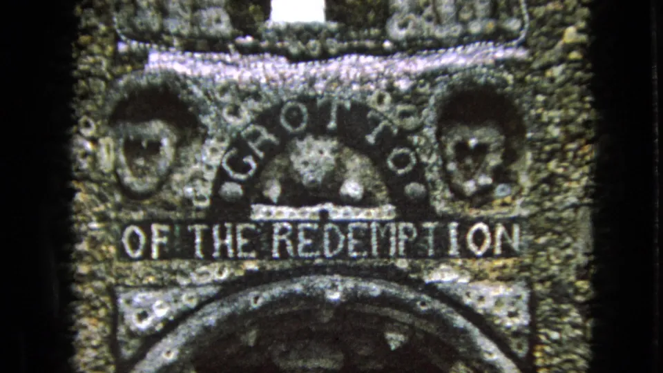 Soft 8mm close-up of the Grotto of the Redemption stone sign in Iowa, showing carved letters, two relief faces, and a curved stone arch beneath.
