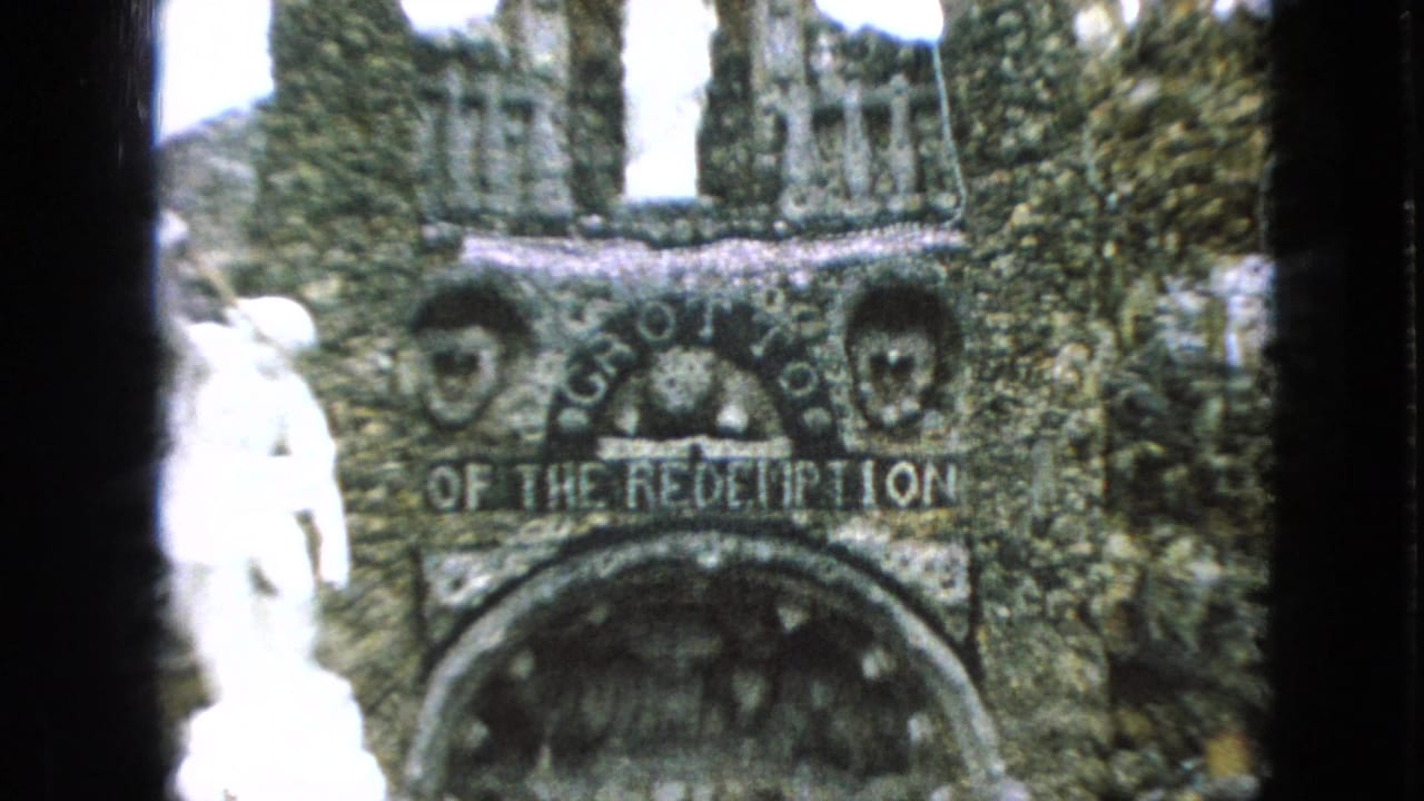 1967 Iowa 8mm frame showing the stone entrance marked Grotto of the Redemption, with a white statue beside the rough rock structure.