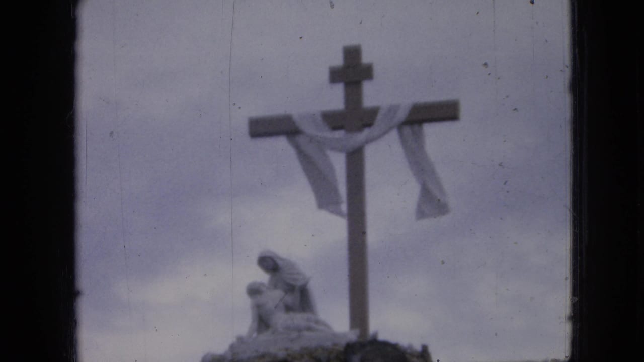 Large outdoor cross with cloth and a small statue-like figure below it.