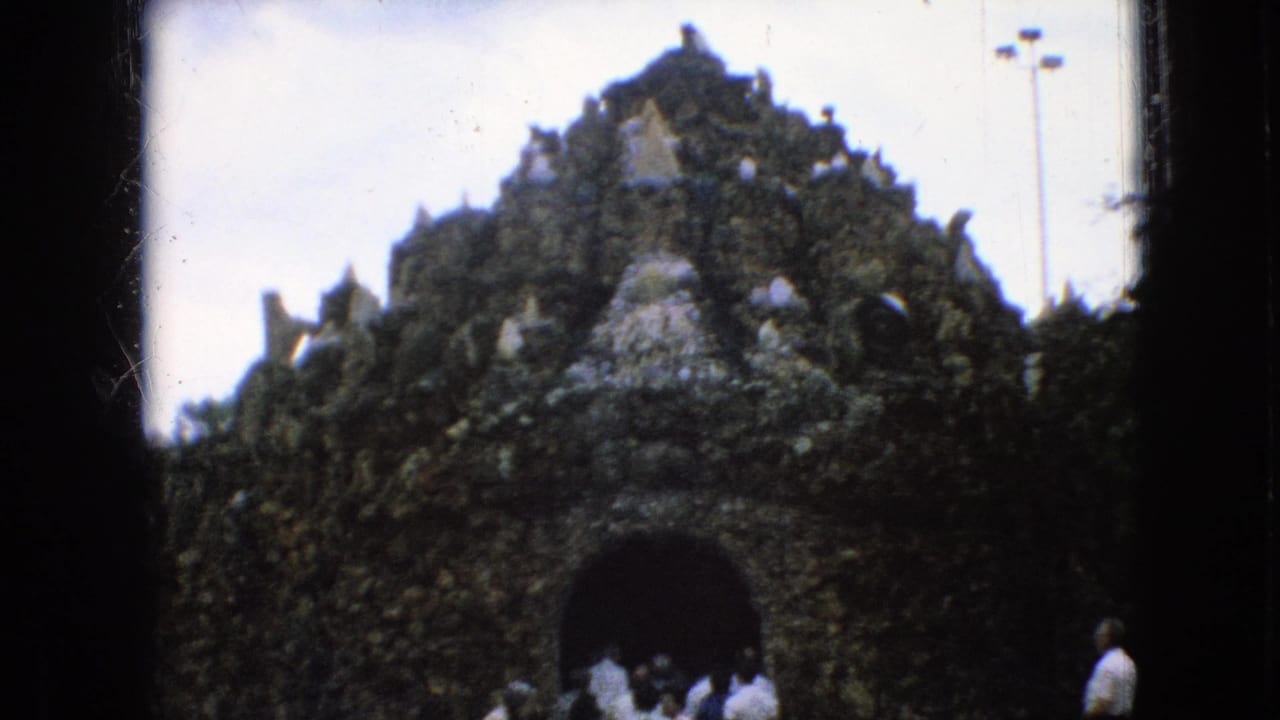 In 1967 Iowa home-movie footage, visitors in casual clothing approach a dark arched entrance set into a rough, rock-like attraction facade with pale crystal accents.
