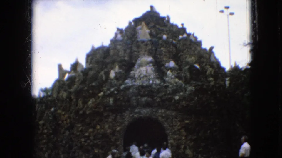In 1967 Iowa home-movie footage, visitors in casual clothing approach a dark arched entrance set into a rough, rock-like attraction facade with pale crystal accents.