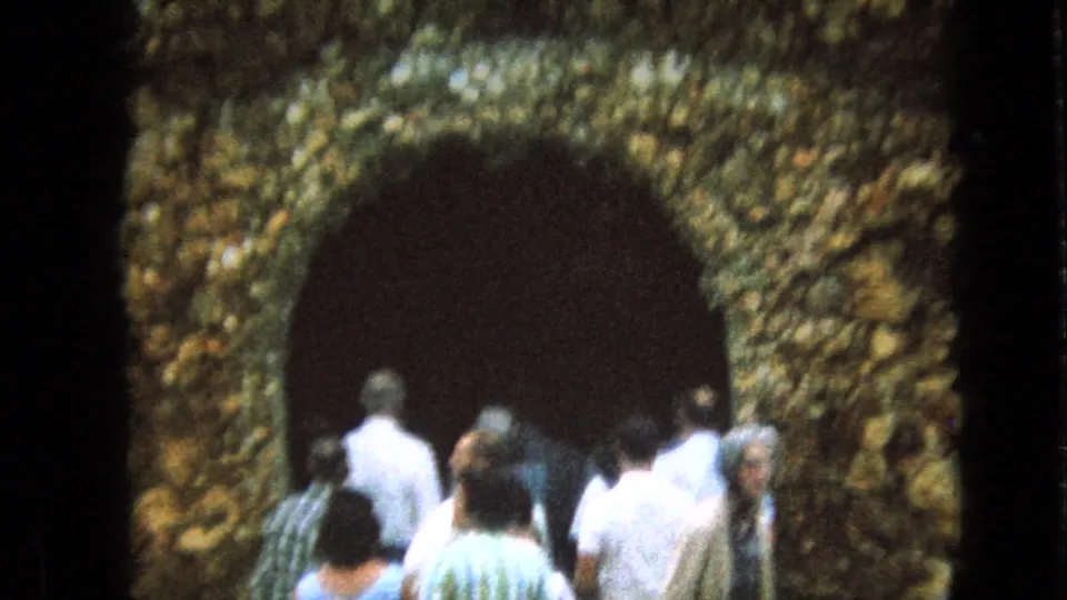 Several visitors in 1960s casual clothing walk into the dark arched entrance of the Iowa cave-like attraction, framed by the rough textured facade.