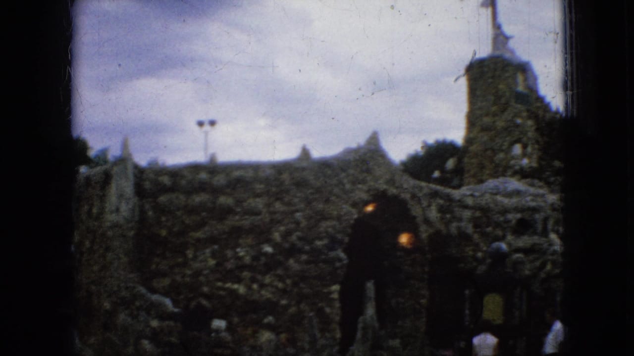 Stone tower with cross above arched openings and visitors near the entrance.