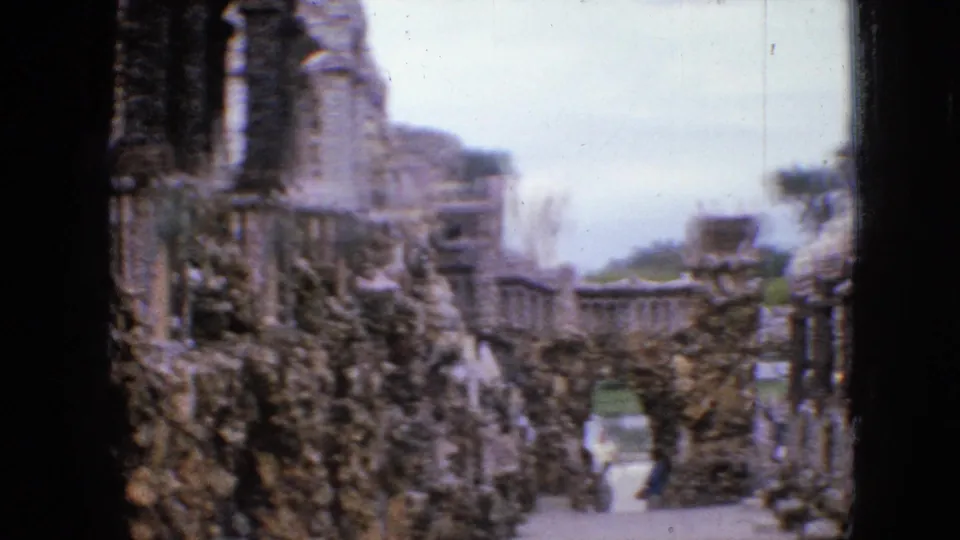 1967 Iowa 8mm frame showing a narrow stone-lined passage through the grotto, with rough masonry walls, a bright sky opening, and a distant visitor figure.