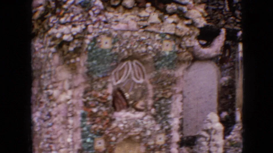 1967 Iowa 8mm frame showing decorative rock and pebble masonry with mosaic-like patterns, arched recesses, and a close handheld view of the handmade structure.
