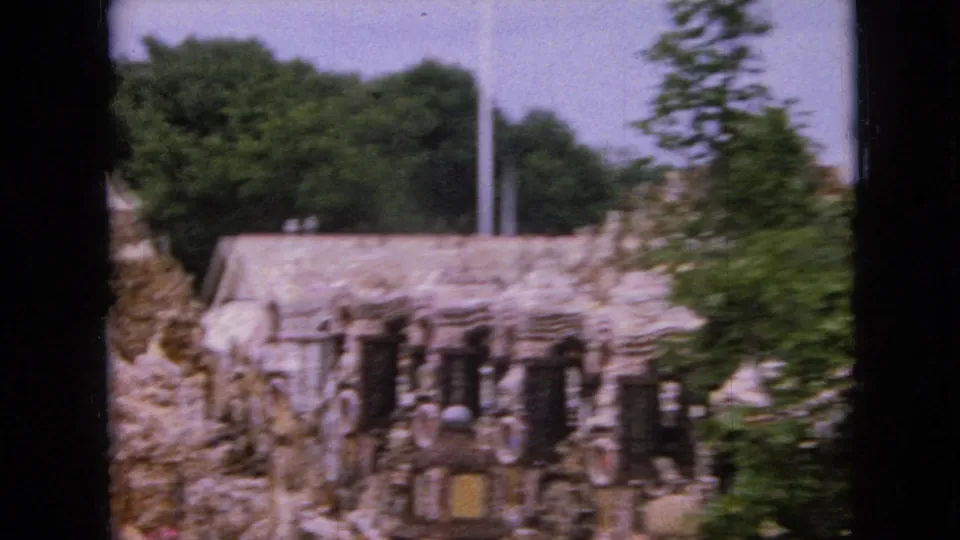 1967 Iowa frame with a closer view of the ornate stone structure, showing columns, rough stonework, surrounding trees, and a dark frame divider.