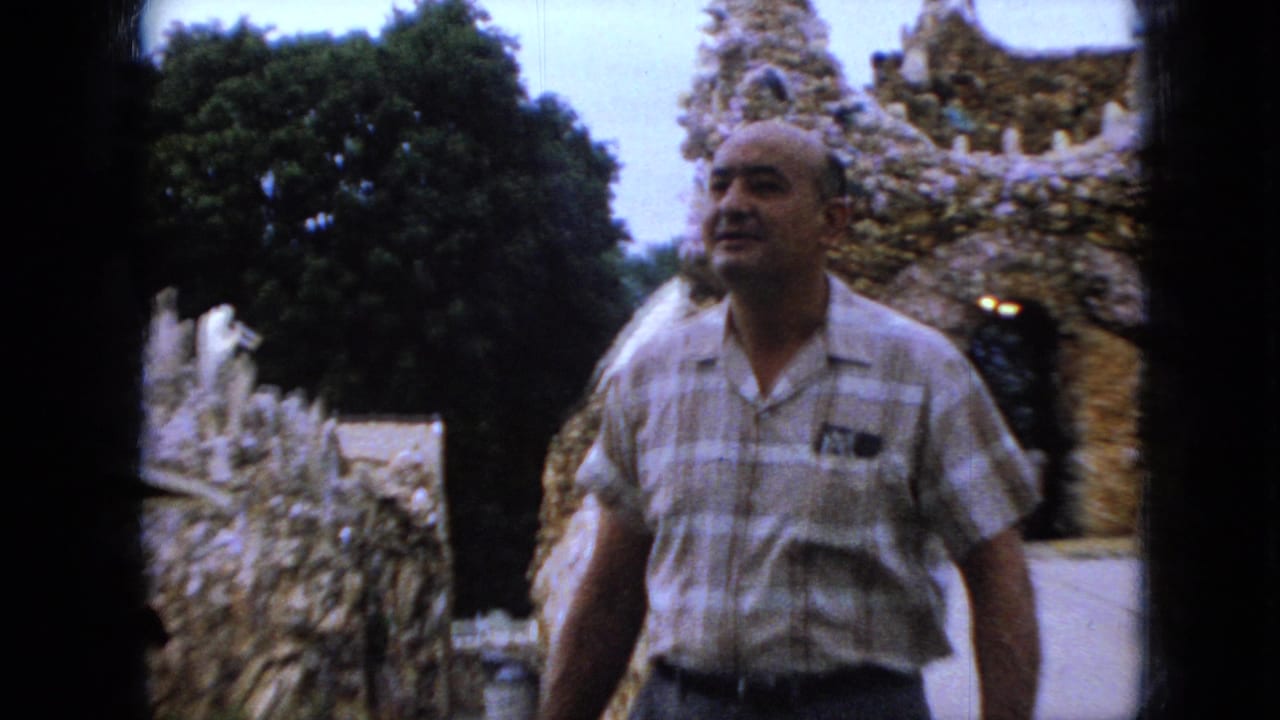 Man in striped shirt passes close to the camera beside rock walls and a mosaic arch.