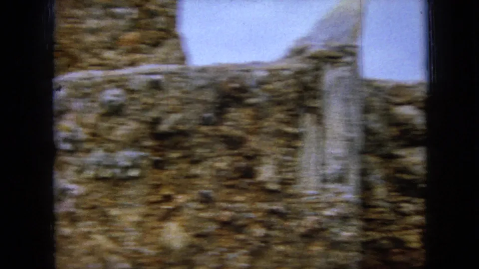 The final frame shows a blurred handheld view of a rock mosaic wall with a pale vertical structural element and bright sky above.