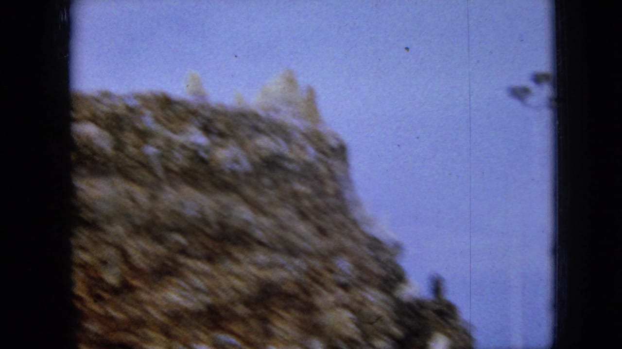 Soft, motion-blurred 1967 Iowa home-movie frame showing a textured stone wall or tower edge against an overcast sky.