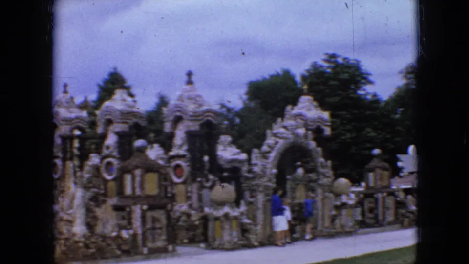 1967 Iowa home-movie view of visitors on a path in front of a whimsical stone landmark with domes, arched openings, crosses, and trees behind it.