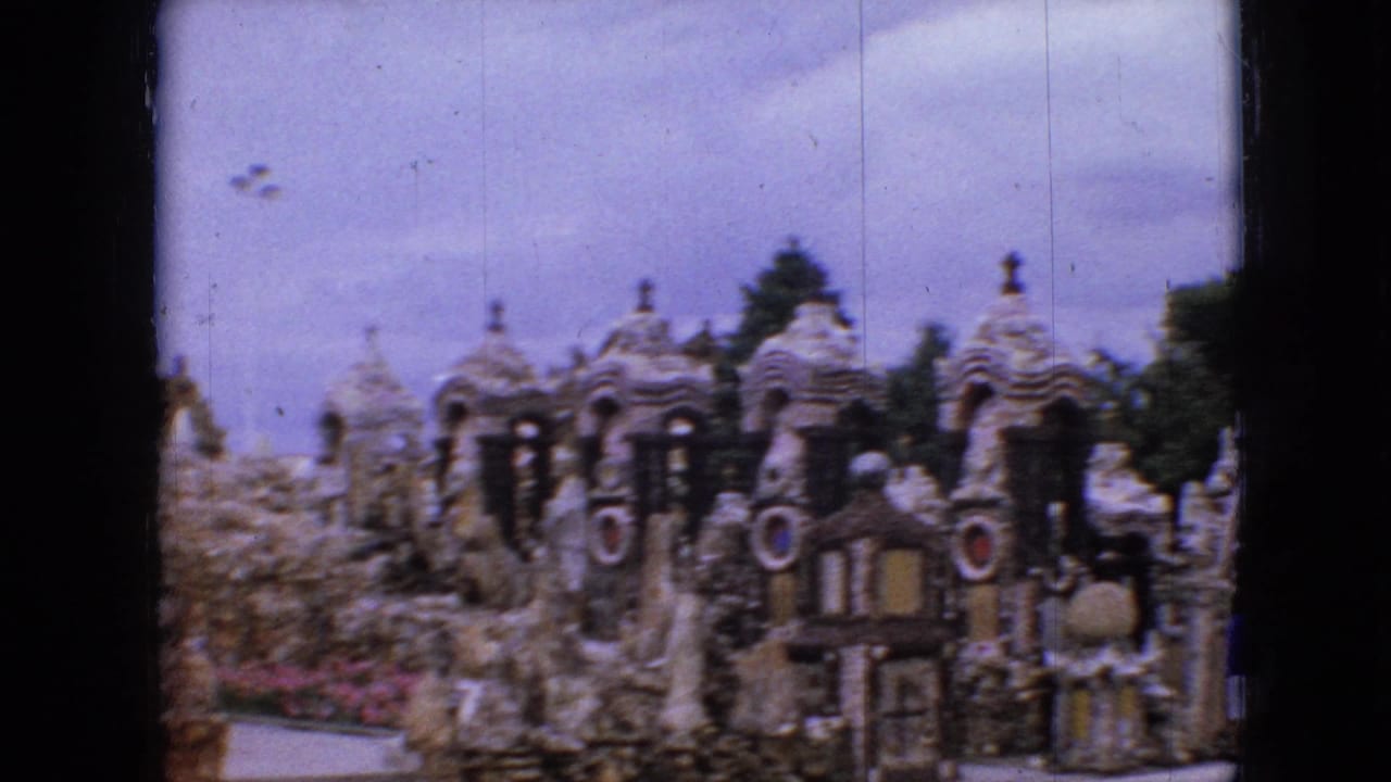 Castle-like stone sculpture garden with decorative turrets and a walkway under an overcast sky.
