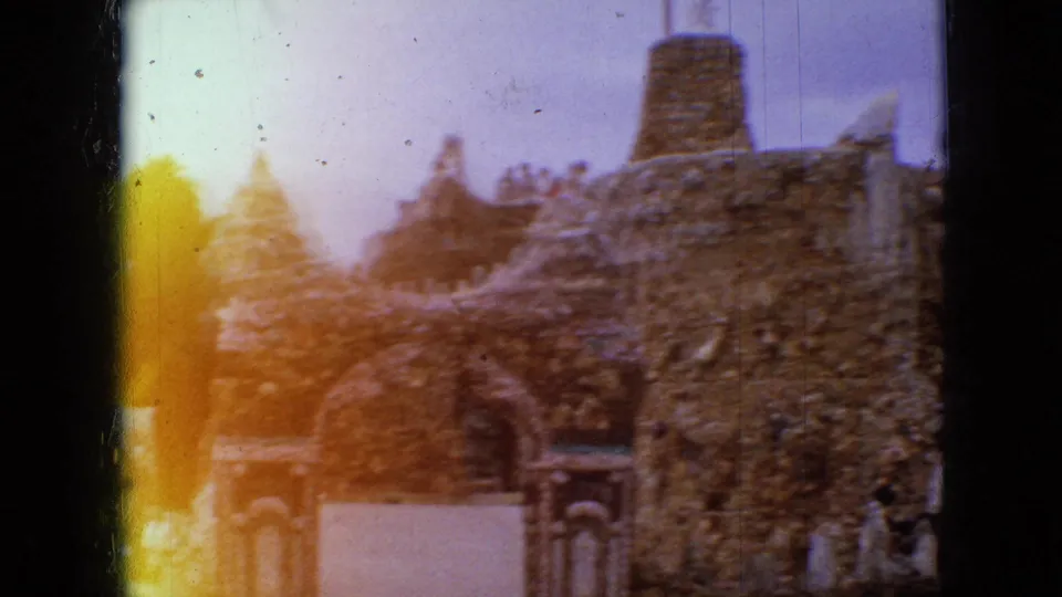 1967 Iowa 8mm frame showing a stone arch and textured wall in the sculpture garden, with strong yellow-orange film exposure flare at the left edge.