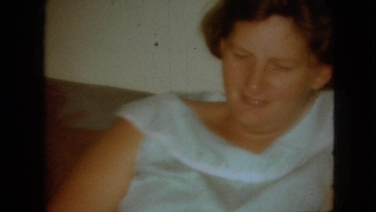 Red-haired woman in a white sleeveless dress looking downward in a soft 8mm frame.