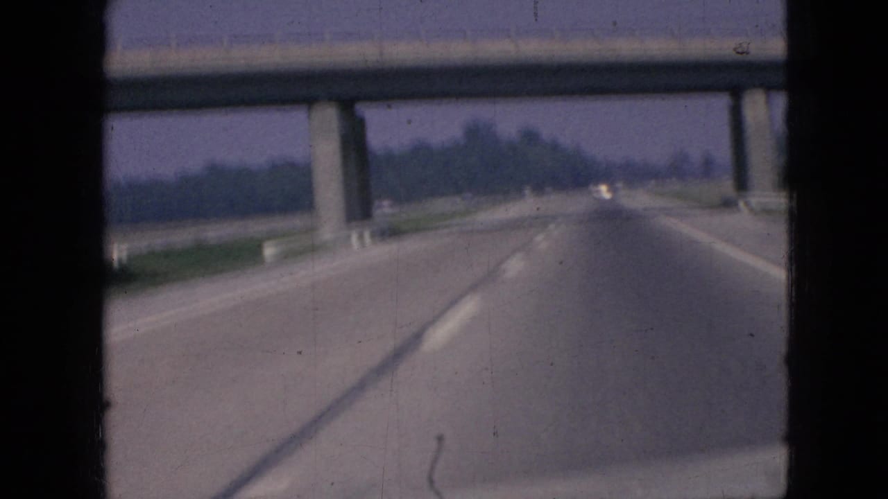 1967 Iowa 8mm road-trip footage looking ahead from inside a vehicle toward a concrete overpass on a multi-lane divided freeway.