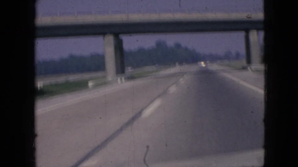 1967 Iowa 8mm road-trip footage looking ahead from inside a vehicle toward a concrete overpass on a multi-lane divided freeway.