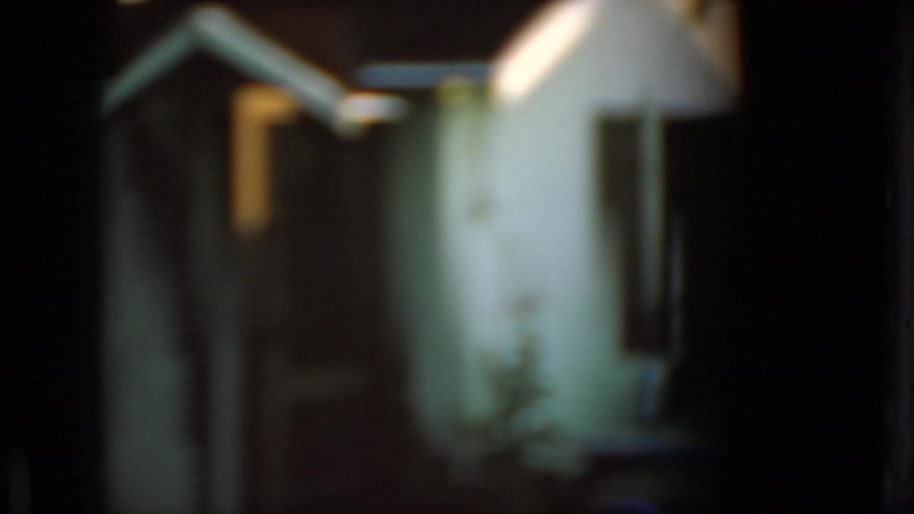 Small light-colored shed or garage with a triangular roof in dim light.