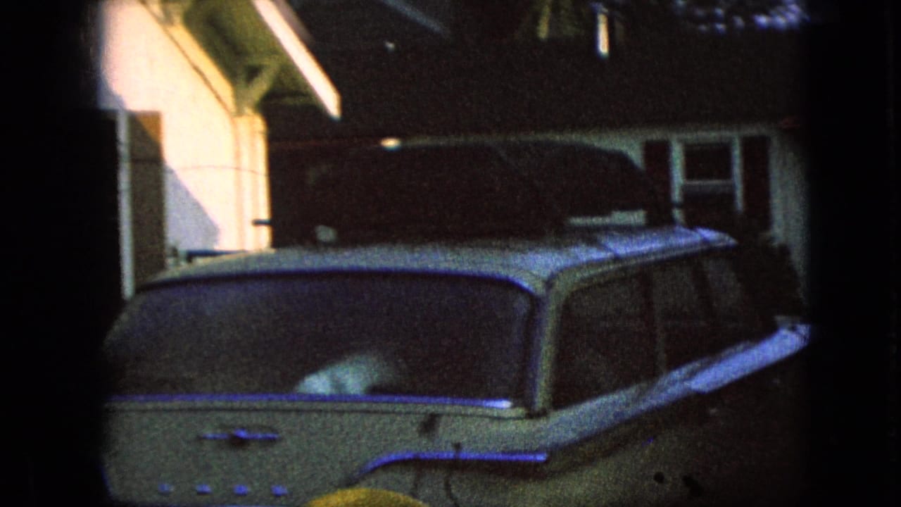 A mid-century station wagon sits near farm structures in 1967 Iowa home-movie footage, with heavy shadow and dark film borders around the frame.